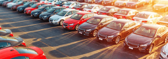 Car dealership lot with rows of vehicles parked in sunlight, illustrating GPS trackers for car dealers and automotive inventory management.