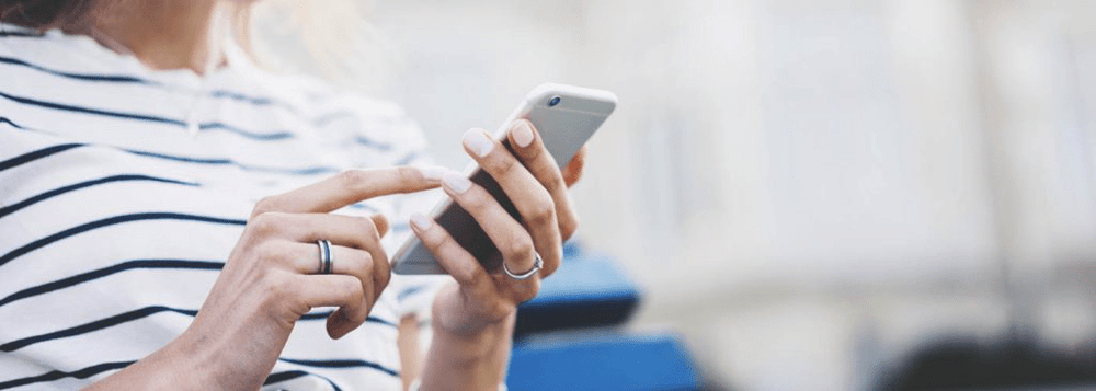 Close-up of a person in a striped shirt using a smartphone outdoors.