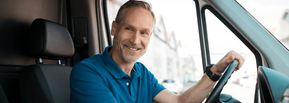 Smiling delivery driver sitting in a van, representing GPS tracking for drivers, fleet management, and business logistics.