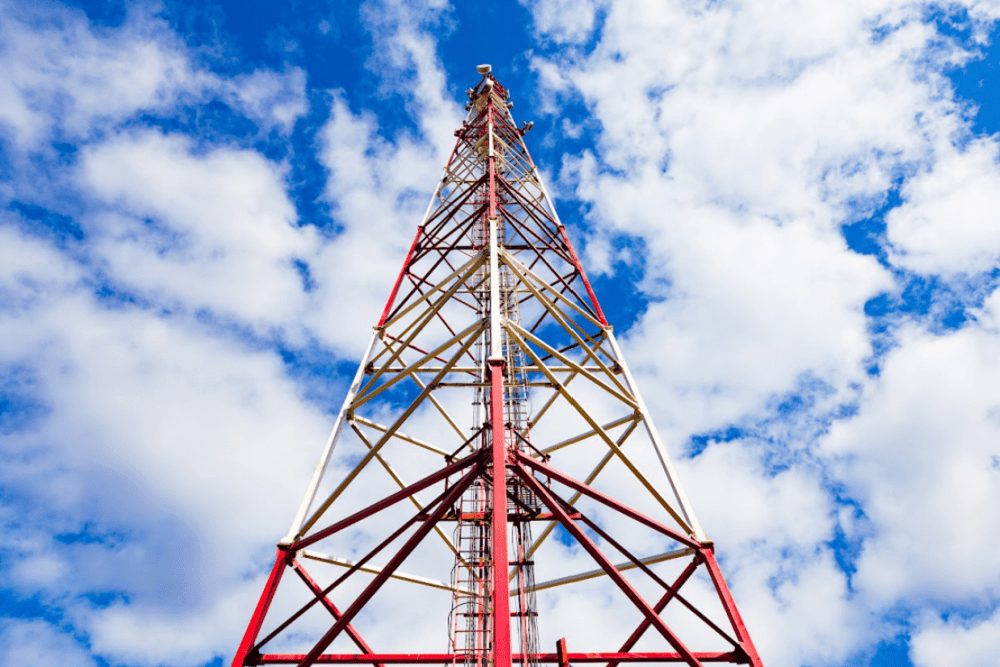 “Red and white cellular tower against a blue sky with clouds, representing GPS tracker connectivity and reliable 4G LTE communication for fleet management.