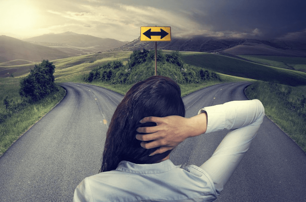Person standing at a crossroads with a road sign pointing left and right, representing the difference between Bluetooth and GPS tracking technology.