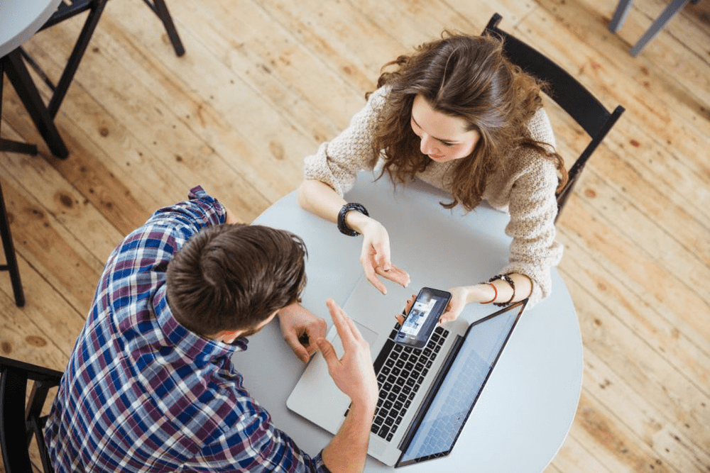 “Two people sitting at a table with a laptop and smartphone, discussing how a GPS tracker works for business and fleet management.