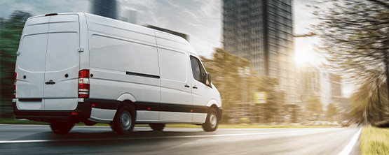 White delivery van driving on a city street, representing GPS shipment tracking and fleet management for businesses.