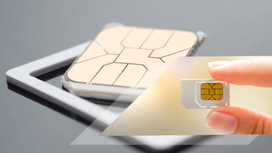 Close-up of a person holding a SIM card with a larger chip in the background, representing SIM cards for GPS trackers and audio monitoring devices.