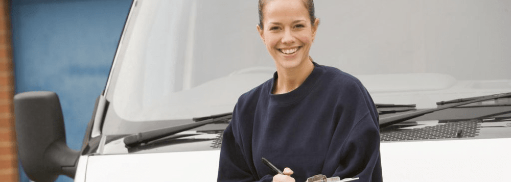 Smiling delivery worker in a navy sweatshirt holding a clipboard, standing in front of a white van.