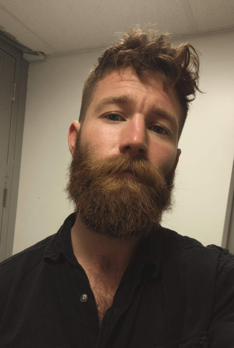 Man with a beard and mustache wearing a black shirt indoors.