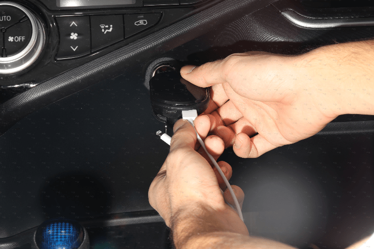 Hands plugging GPS tracking device into a car’s USB power port for real-time vehicle tracking.