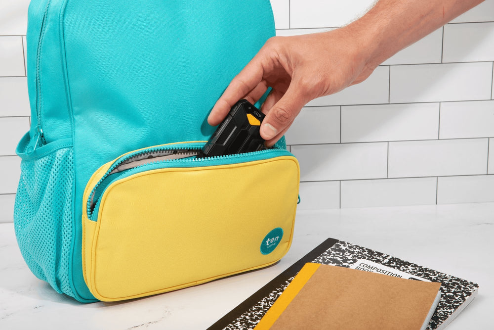 Turquoise and yellow backpack with a hand placing an item inside, on a white tiled floor.