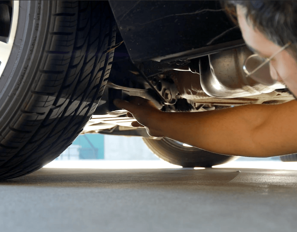 Person installing a GPS tracking device under a car near the rear wheel for discreet vehicle monitoring.