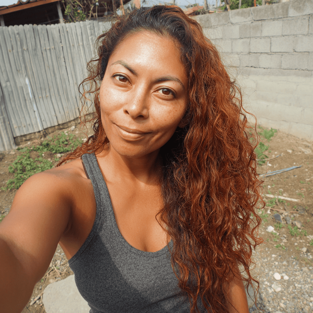 Woman takes selfie in backyard with brick wall behind her.