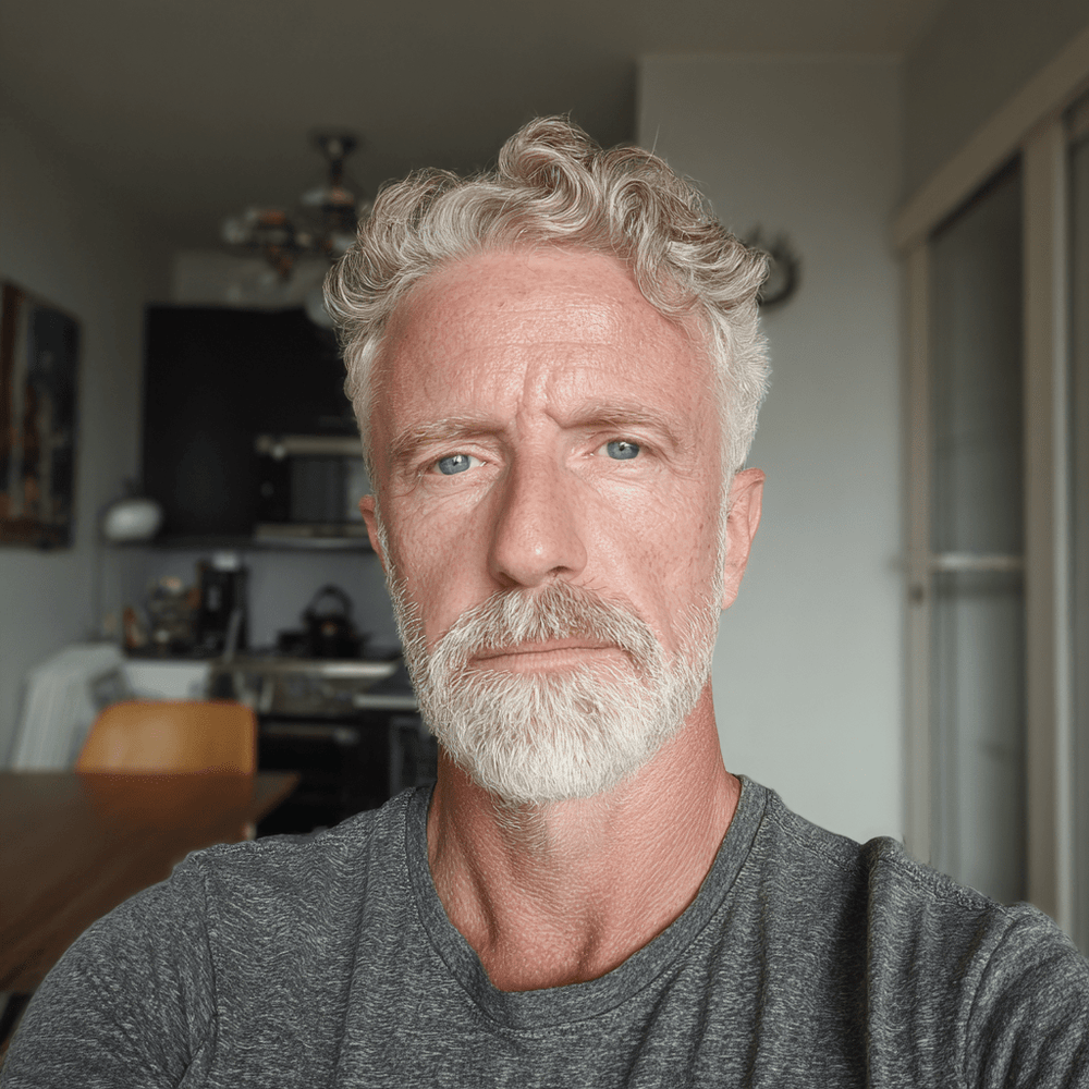 Man with gray hair and beard wearing a gray shirt in an indoor setting