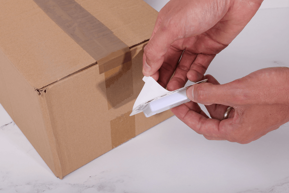 Person peeling adhesive off GPS device to attach to shipment
