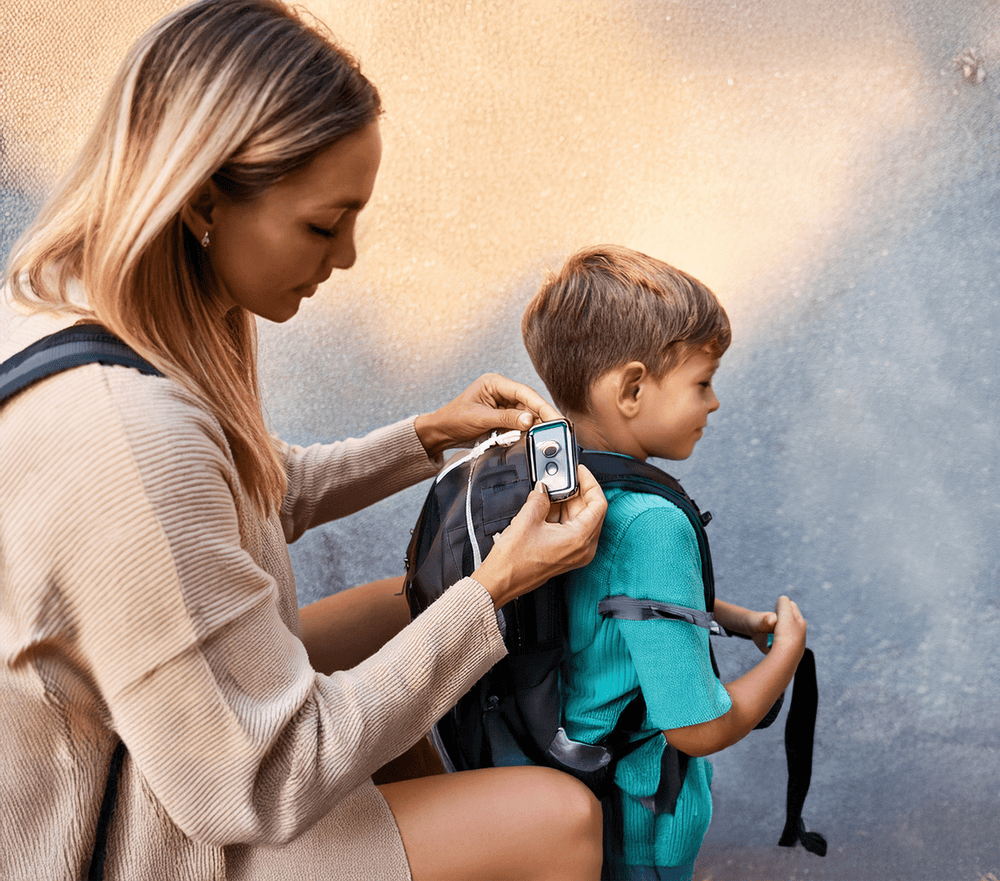 Mother attaching a GPS tracking device to her child’s backpack to ensure safety and provide peace of mind during school commutes.