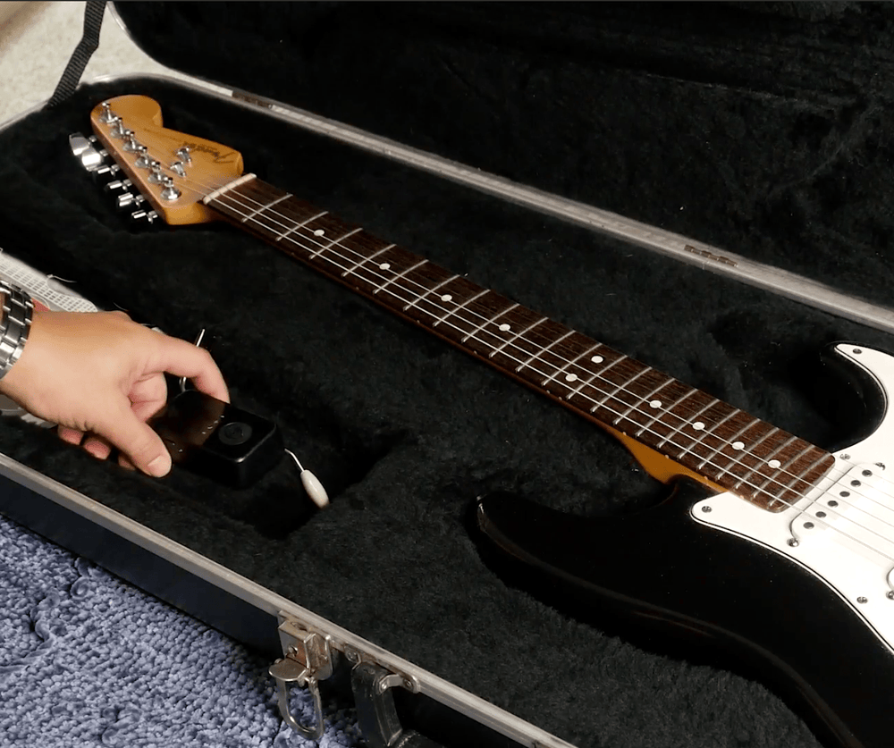 Hand placing a GPS tracking device inside a guitar case with an electric guitar, showcasing secure asset protection for musical instruments.