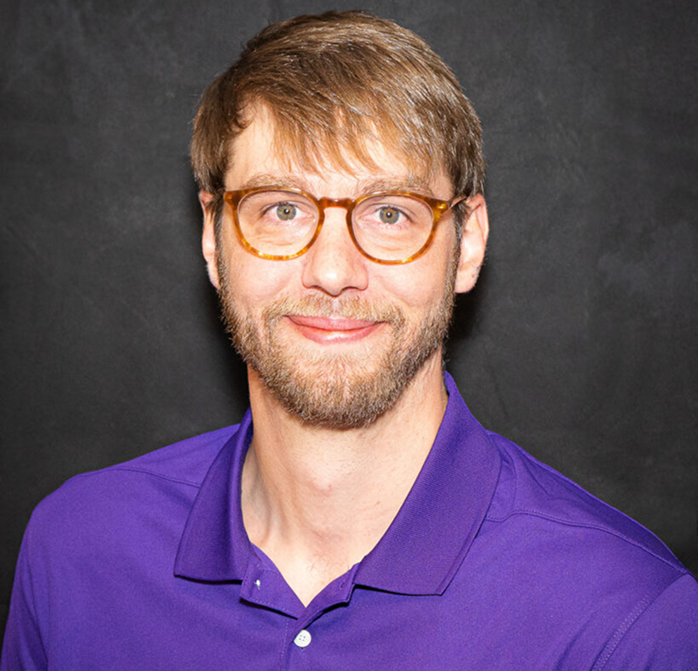 Man wearing glasses and a purple shirt against a black background