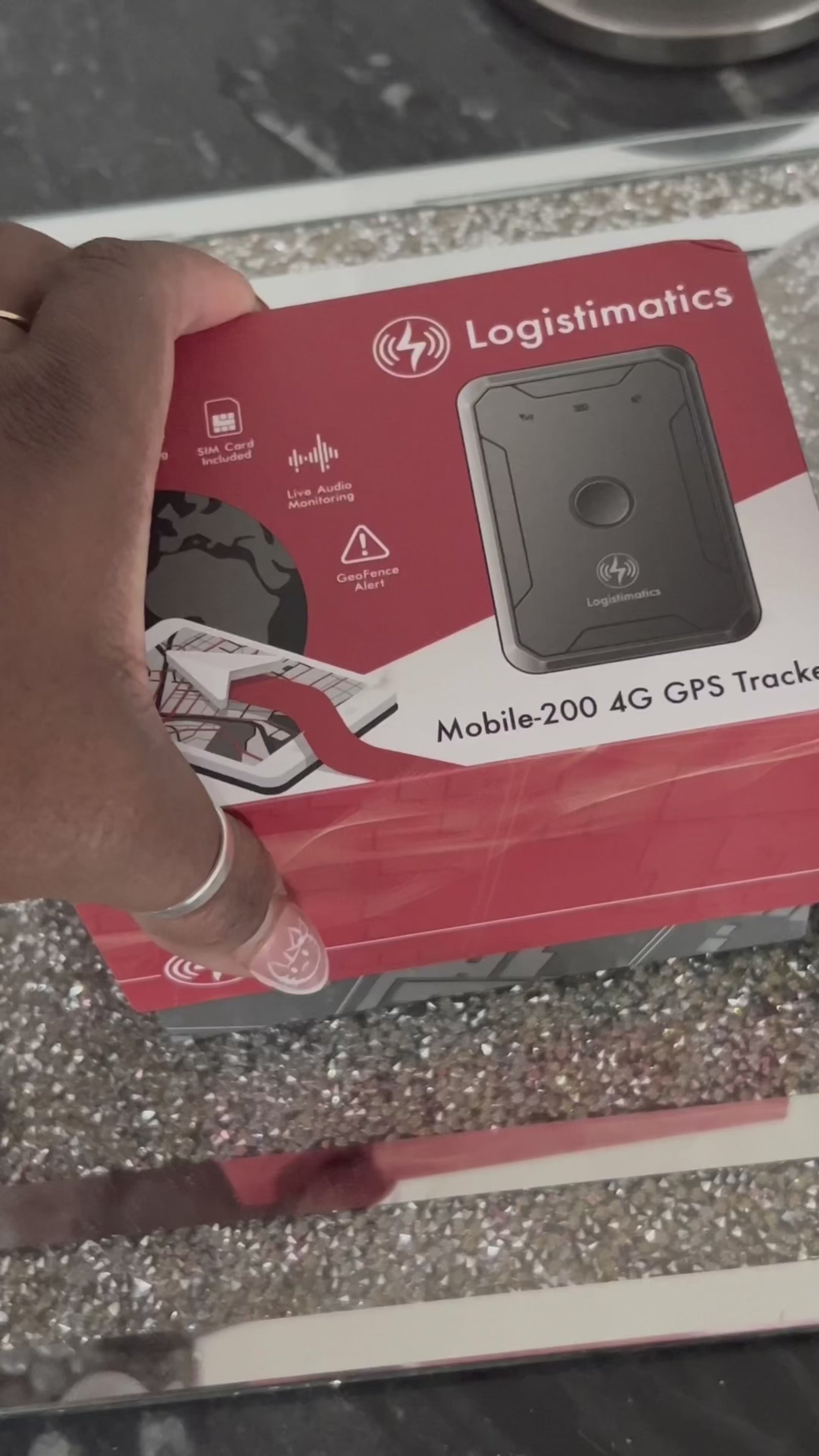 A person is shown in a domestic setting with a small tracking device in a video that likely discusses the user-friendly aspects of the tracker for ensuring safety through real-time updates.